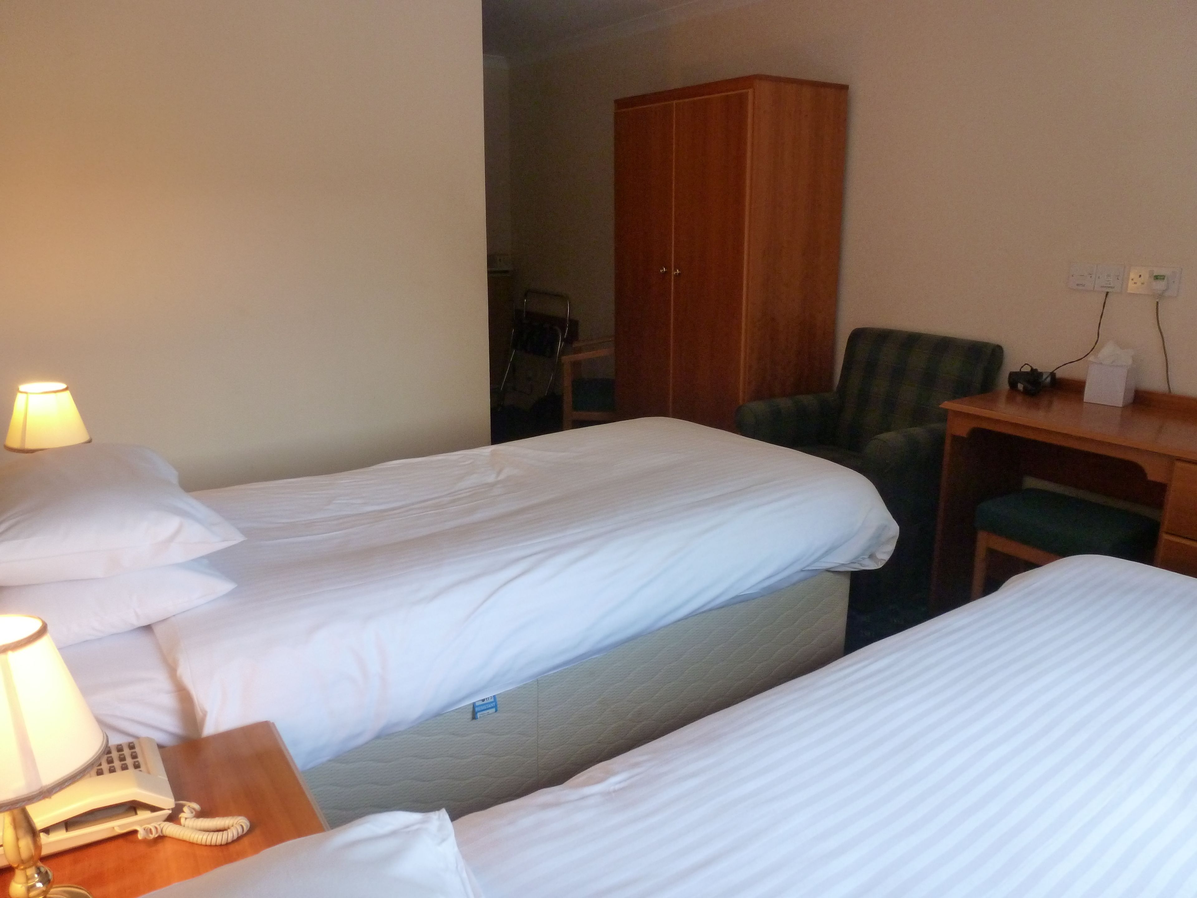 A hotel room with two single beds, a desk, a chair, and a wardrobe.