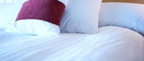 A bed with white bedding and a single red pillow.