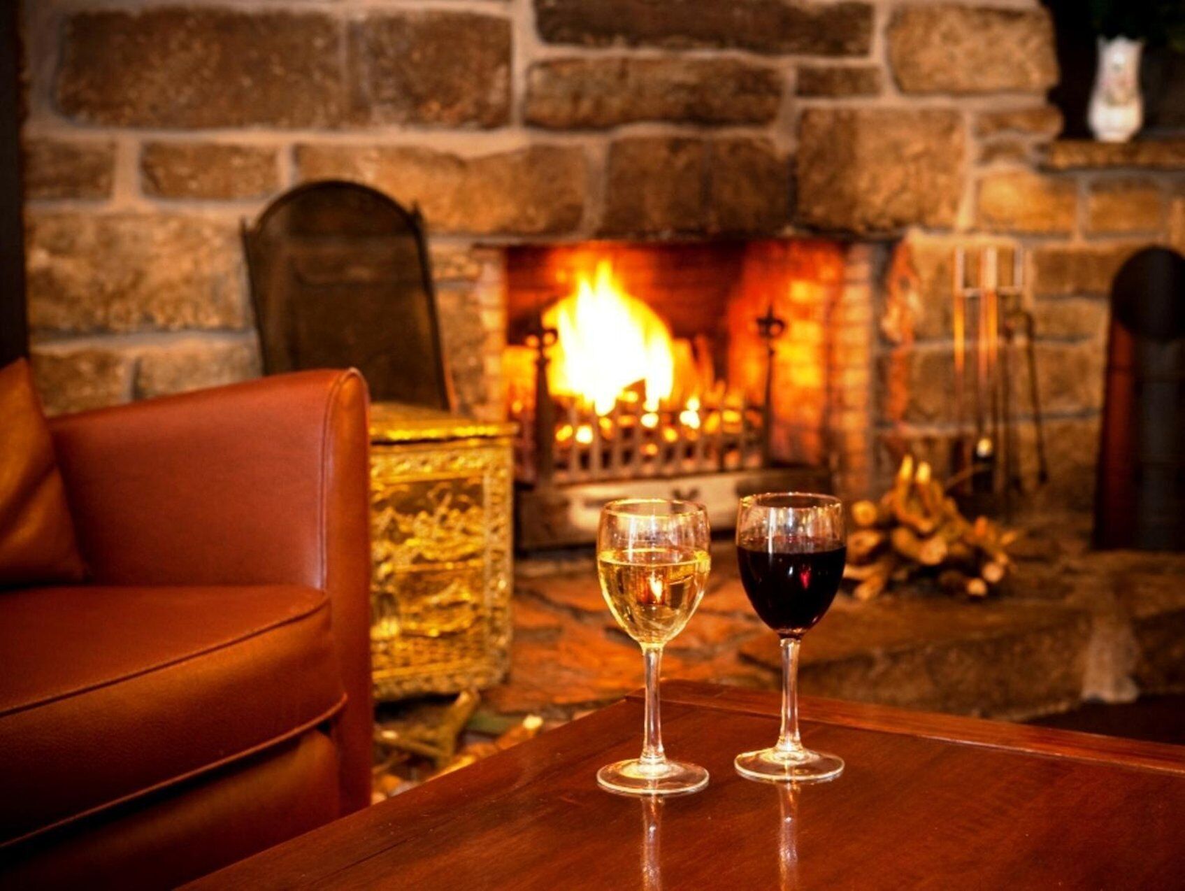 A cozy room with a stone fireplace, leather armchair, and two glasses of wine on a wooden table.