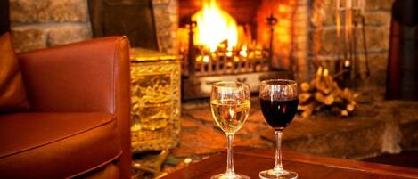 A cozy room with a stone fireplace, leather armchair, and two glasses of wine on a wooden table.
