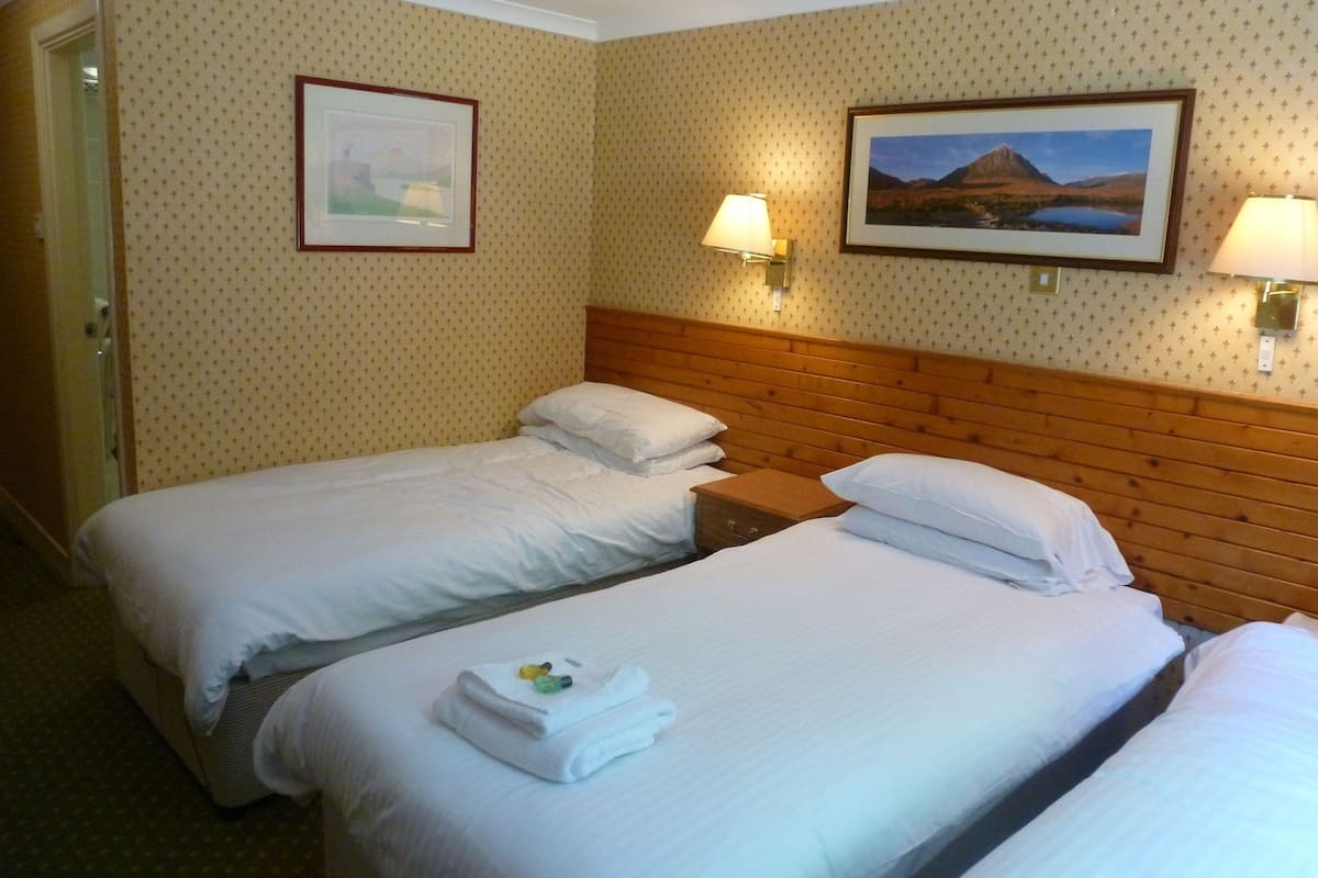 A hotel room with two beds, a wooden headboard, wall-mounted lamps, and framed pictures.