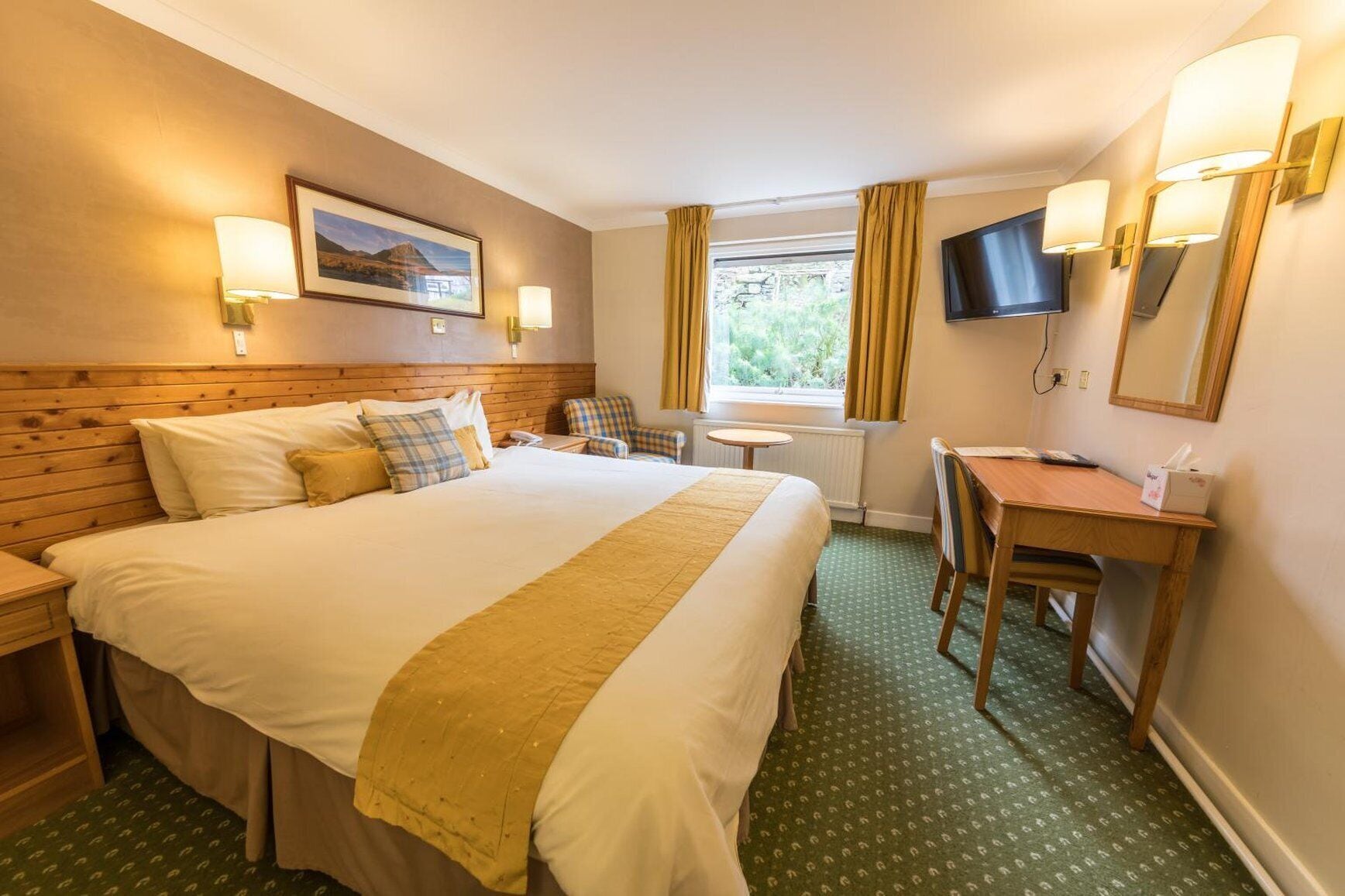 A hotel room with a large bed, a desk, a chair, a TV, and a window with curtains.