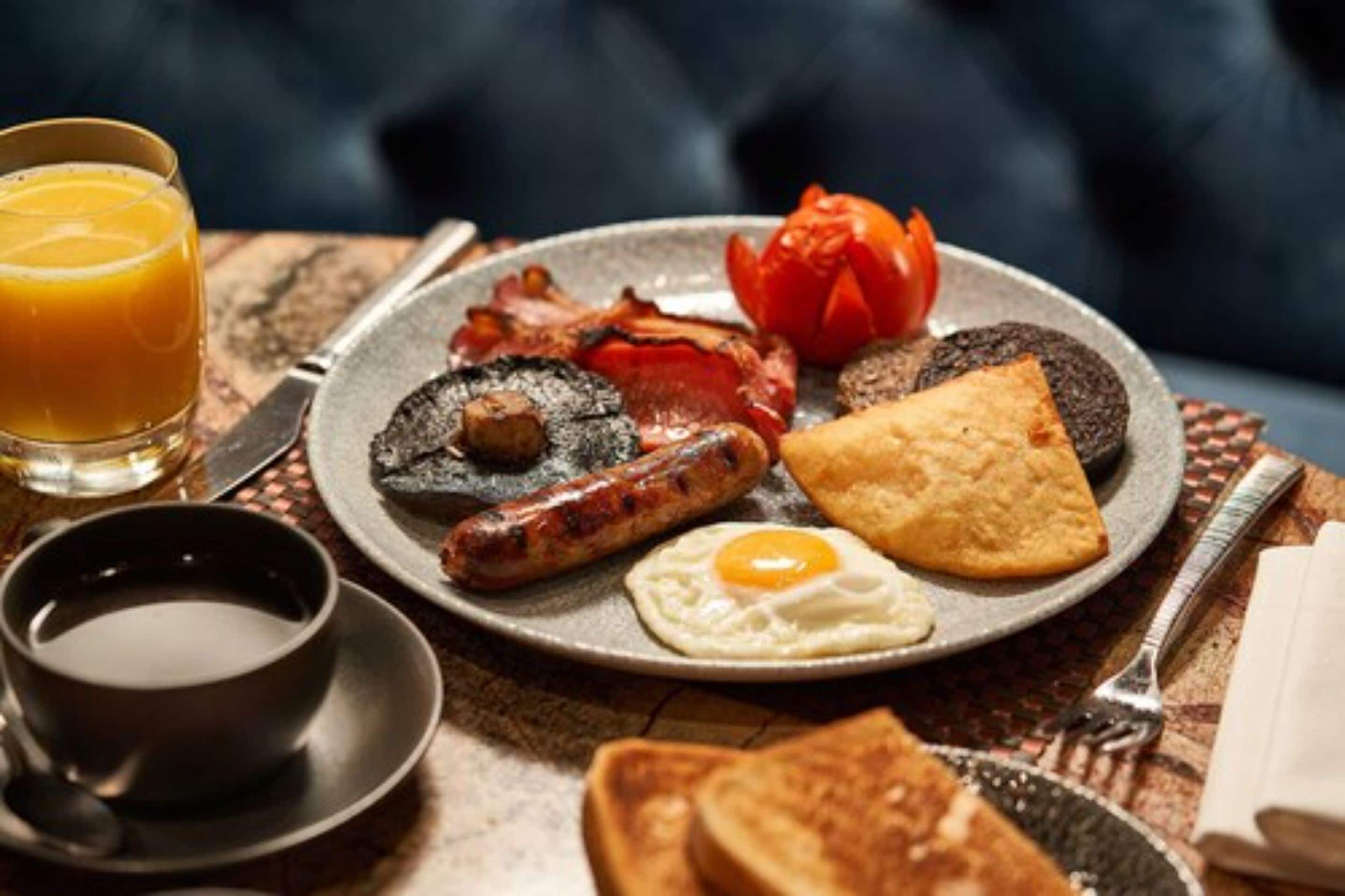 Une assiette de petit-déjeuner comprenant du bacon, des saucisses, des œufs, des toasts et une tomate.