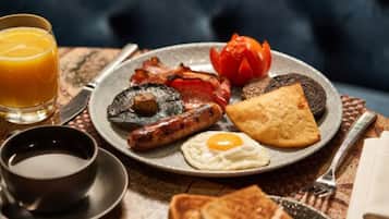 Une assiette de petit-déjeuner comprenant du bacon, des saucisses, des œufs, des toasts et une tomate.