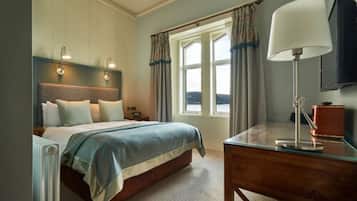 Un dormitorio con cama, lámparas de noche, un escritorio con lámpara, una ventana con cortinas y vistas al exterior.