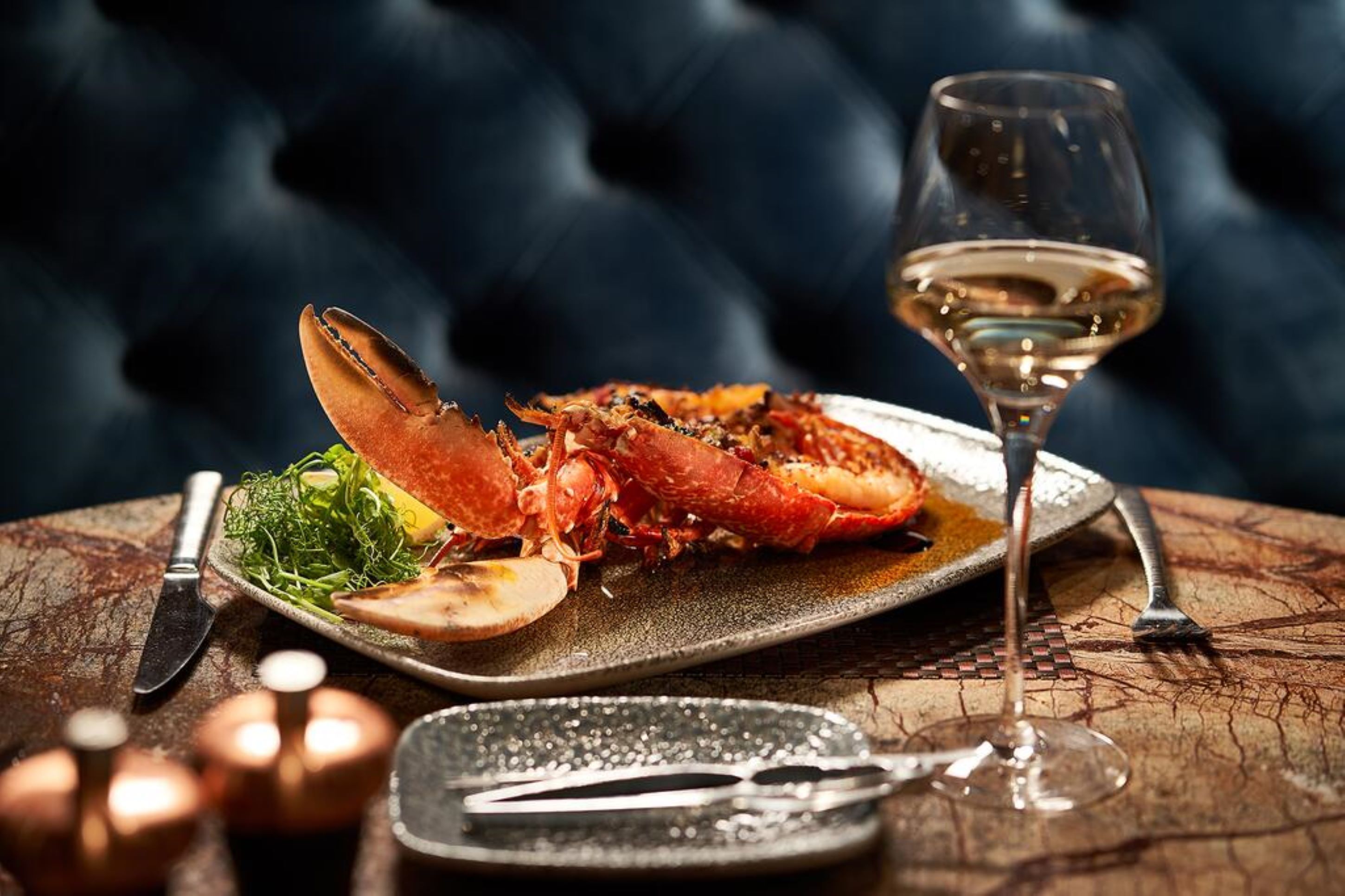 A lobster dish on a plate with a glass of white wine, set on a wooden table.