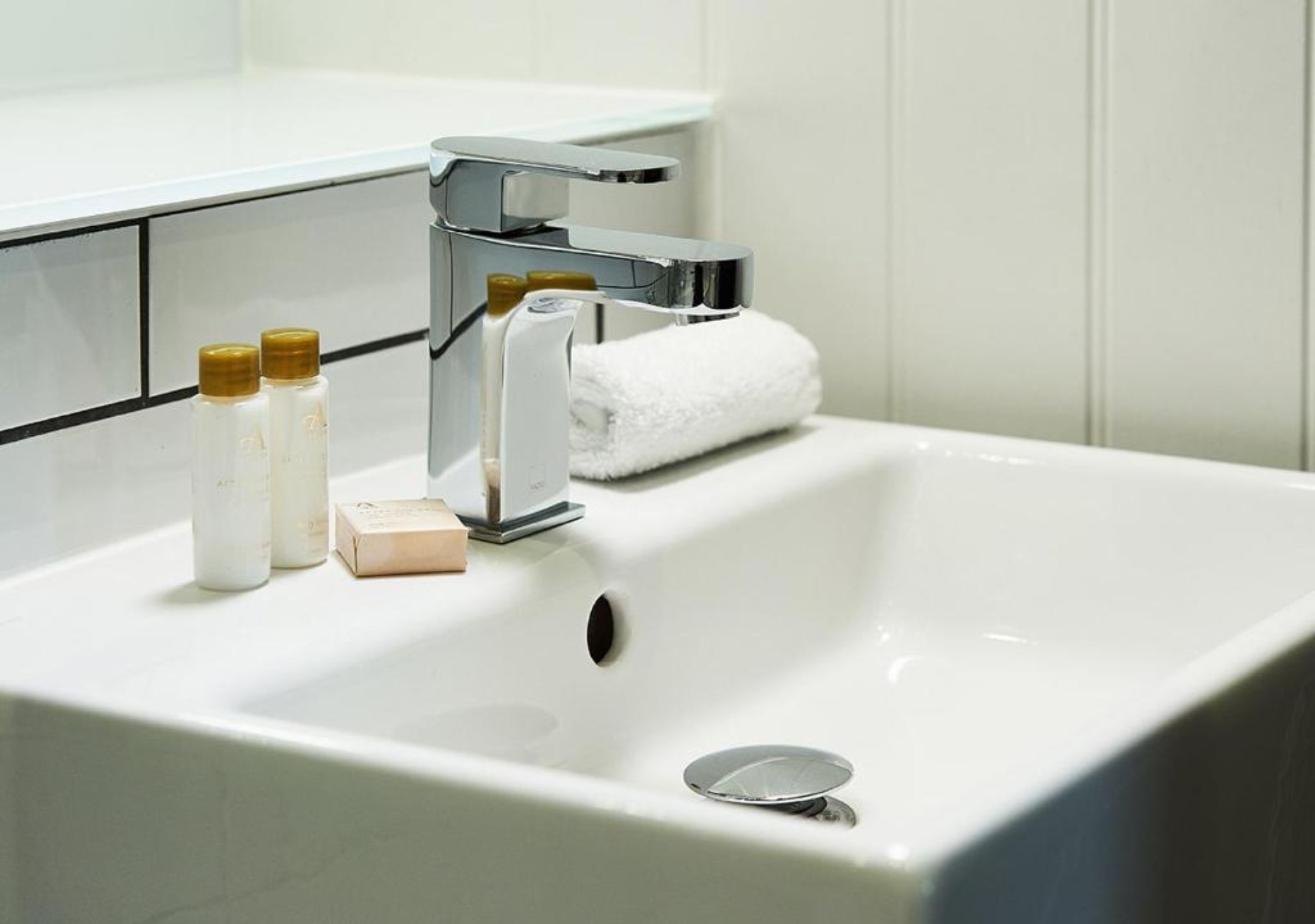 A white bathroom sink with a chrome faucet, a white towel, and three toiletries.