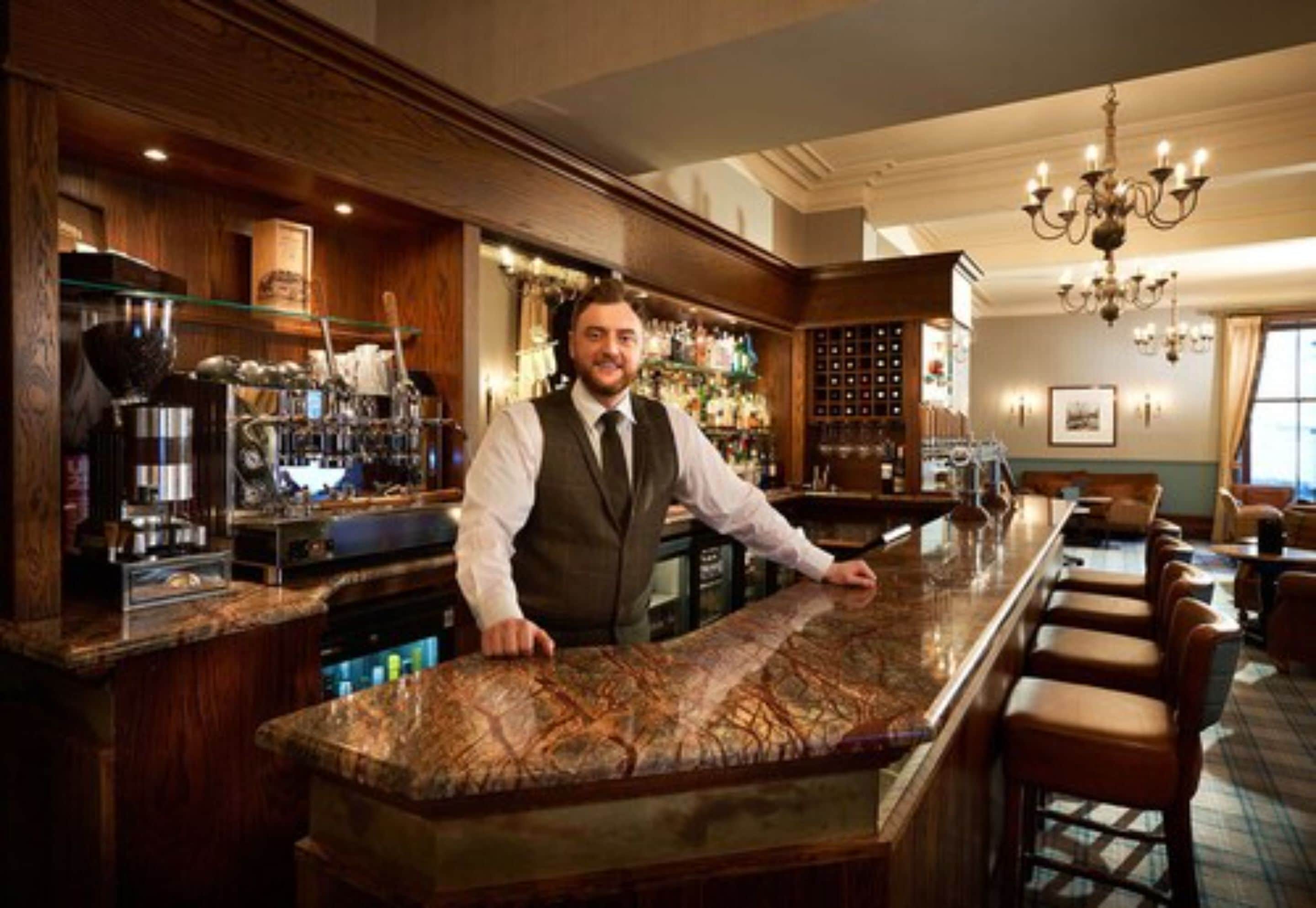 Un espace bar doté d’un comptoir en marbre, de tabourets de bar en bois et d’un barman.