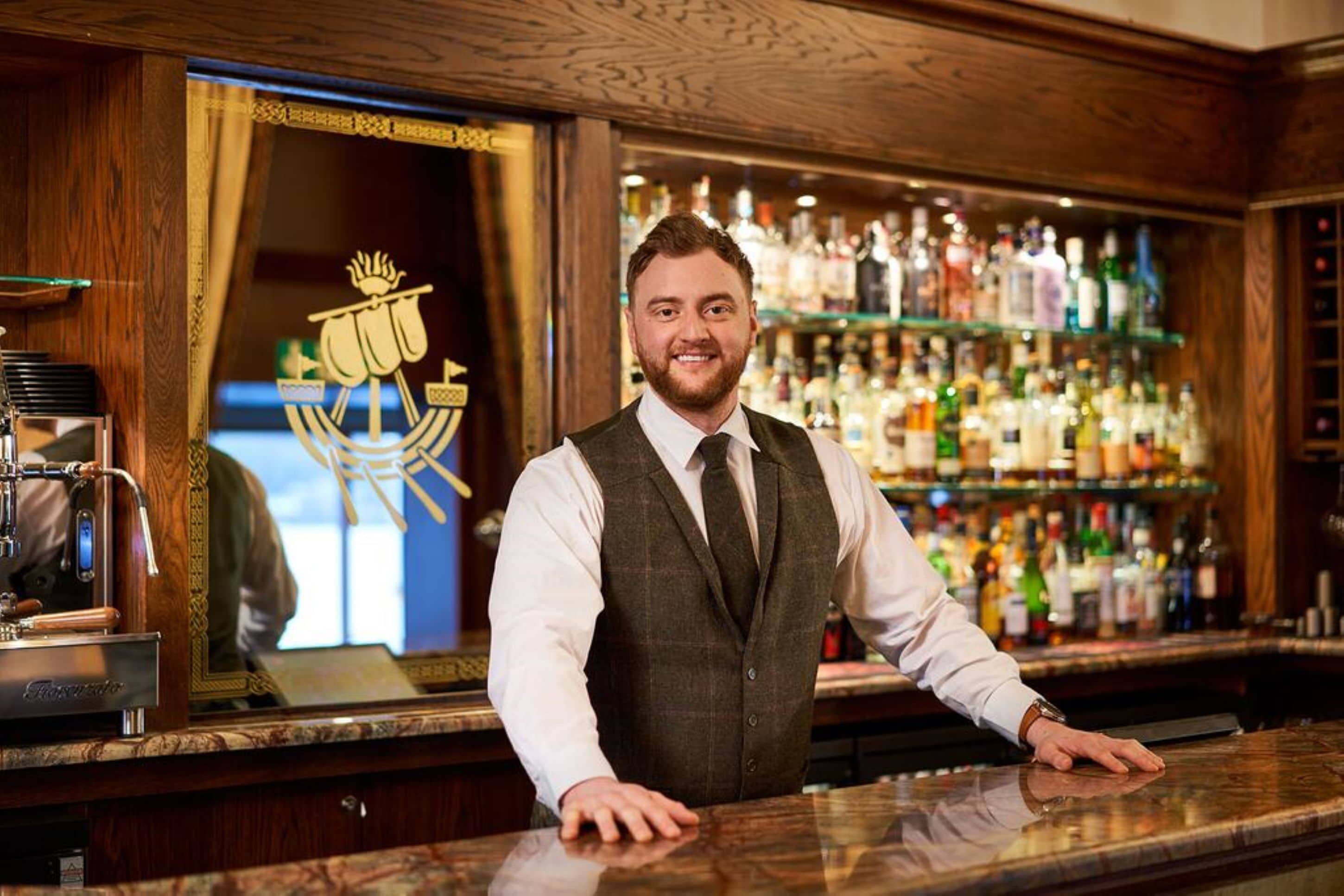A bar with a wooden interior, a large mirror reflecting the bar area, and shelves stocked with various bottles.