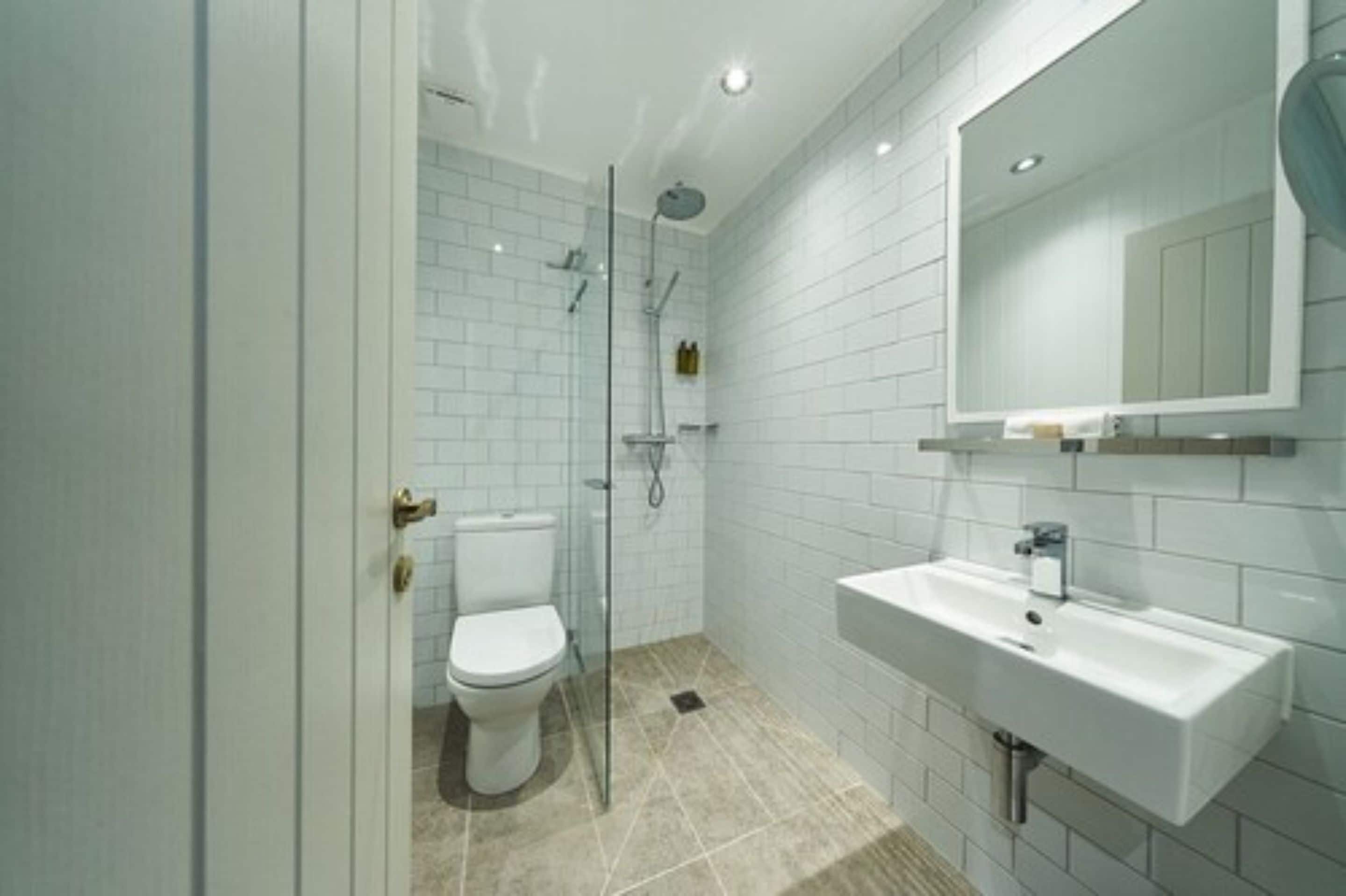 Une salle de bain moderne avec des carreaux blancs, une douche en verre, des toilettes et un lavabo surmonté d’un miroir.