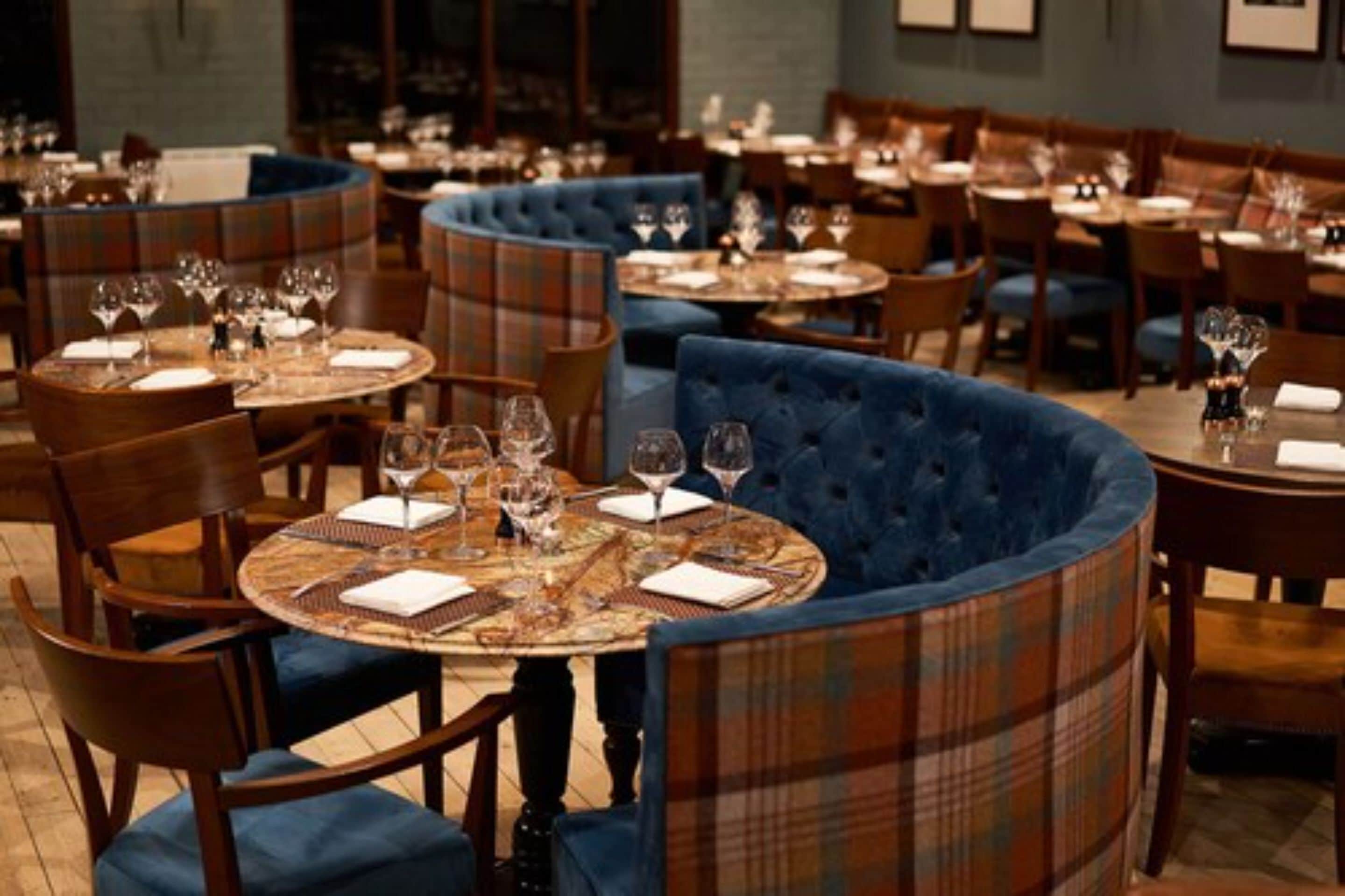 A restaurant with round tables and blue upholstered booths, featuring a plaid pattern.