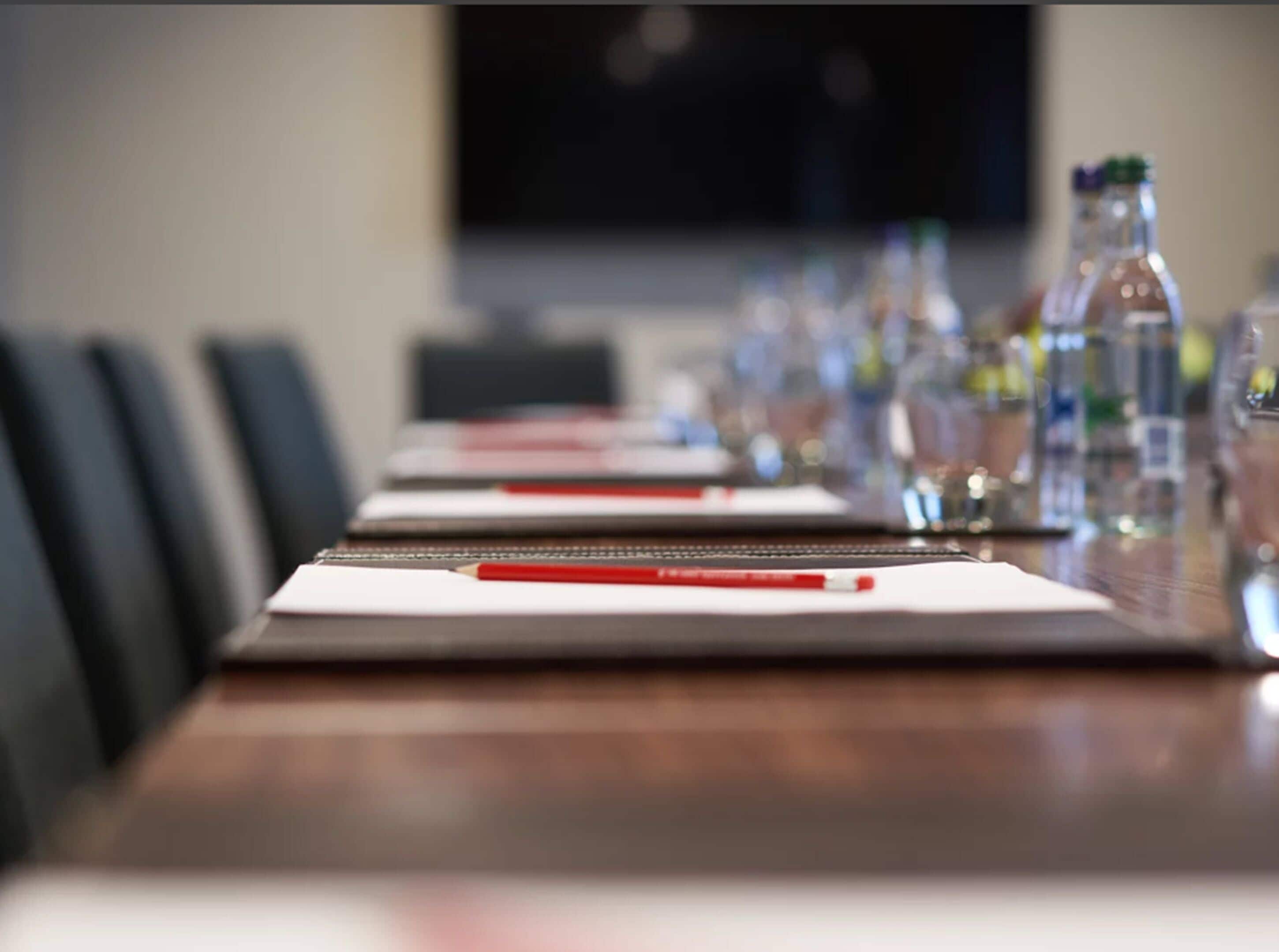 Un salón de conferencias con una larga mesa dispuesta para reuniones, equipado con tarjetas de identificación, bolígrafos y botellas de agua.