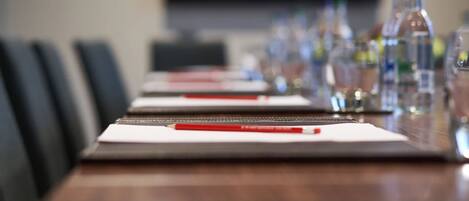 Un salón de conferencias con una larga mesa dispuesta para reuniones, equipado con tarjetas de identificación, bolígrafos y botellas de agua.