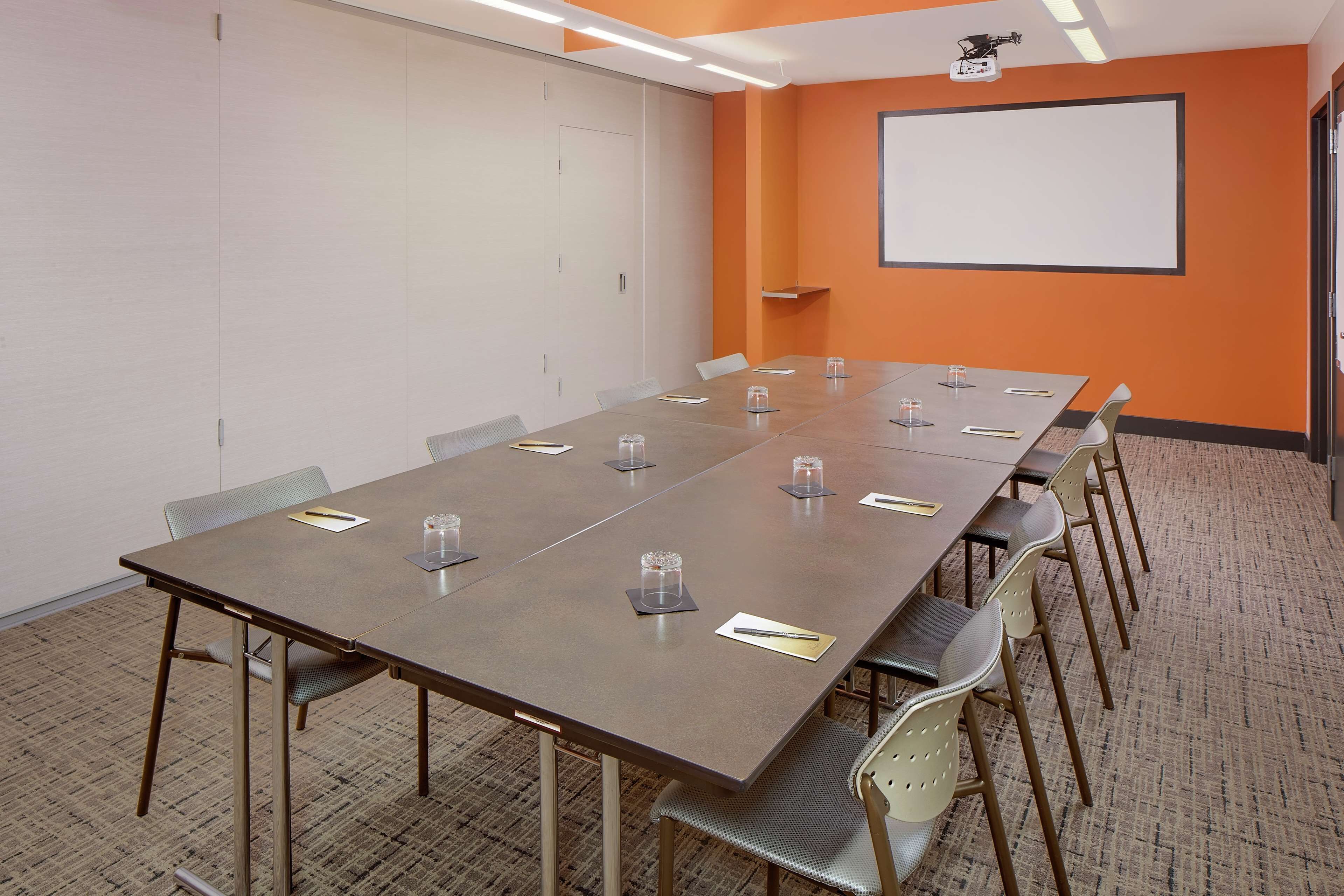Un salón de conferencias con una larga mesa, sillas, una pantalla de proyector y piso alfombrado.