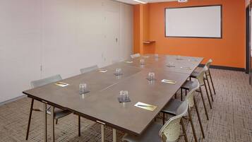 Un salón de conferencias con una larga mesa, sillas, una pantalla de proyector y piso alfombrado.