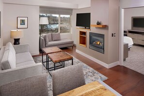 A modern living room with a grey sofa, a wooden coffee table, a fireplace, and a television mounted on the wall.