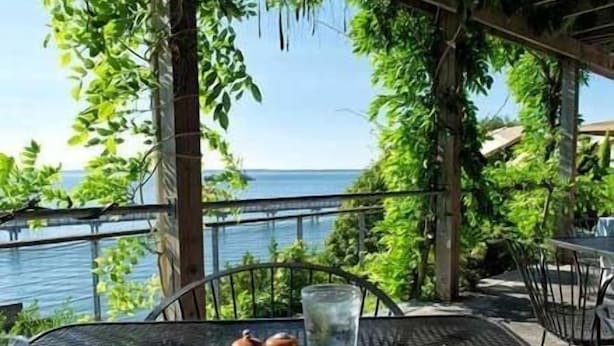 Une table dressée avec un repas, un verre d’eau et des salières et poivrières, donnant sur une étendue d’eau.