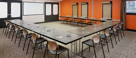 A conference room with a long table, chairs, a projector screen, and a clock on the wall.