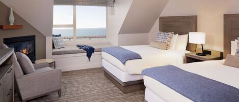 A hotel room with a fireplace, two beds, a sofa, and a view of the sea.