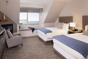 A hotel room with a fireplace, two beds, a sofa, and a view of the sea.