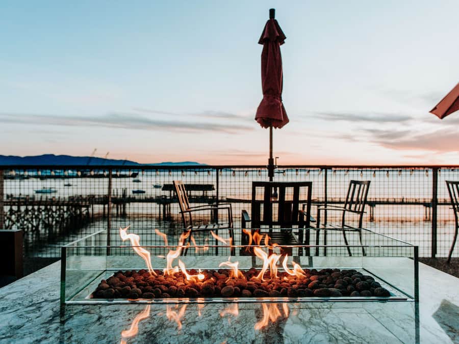 A glass-top table with a fire feature, outdoor chairs, and a view of the sea at sunset.