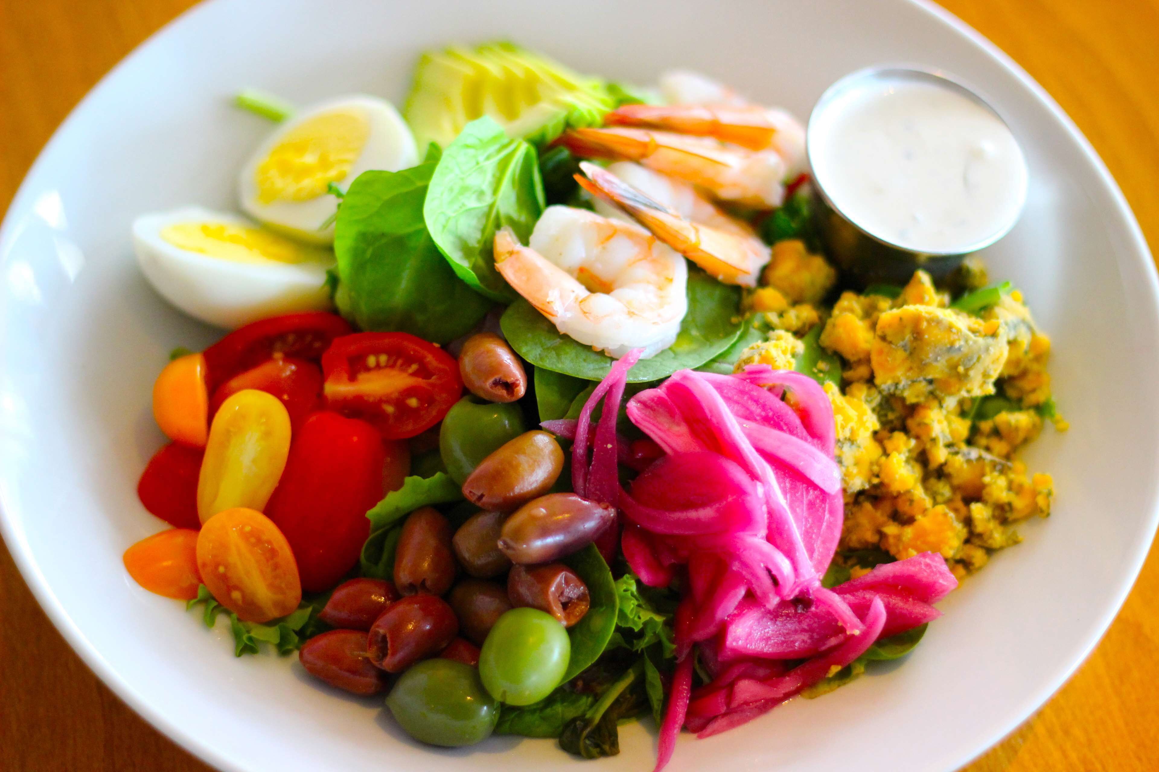 Een salade met diverse ingrediënten, zoals sla, tomaten, olijven en garnalen.