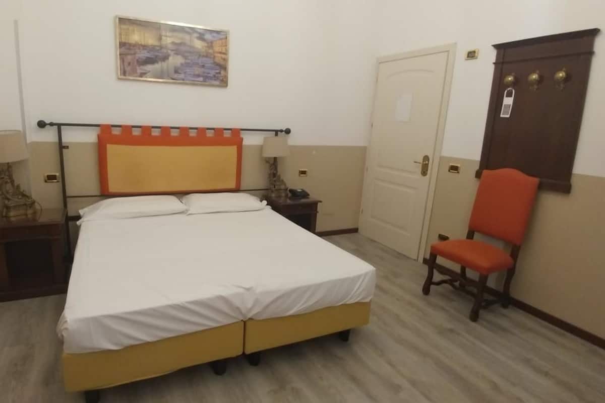 A hotel room with a bed, two bedside tables, a chair, a door, and a painting on the wall.