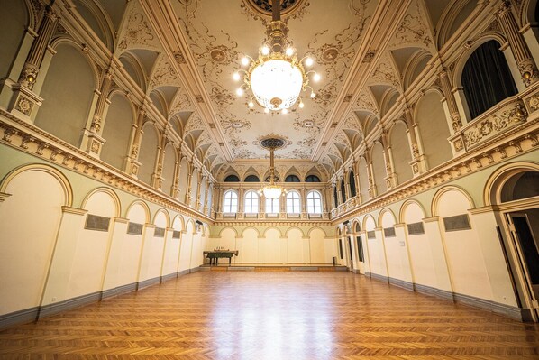 Un salón imponente con techo ornamentado, amplias ventanas y un candelabro.