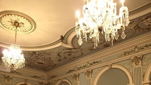 A formal dining room with ornate chandeliers, high ceilings, and classical architecture. Tables are set with white tablecloths and gold napkins. - Tisza Hotel (Szeged)