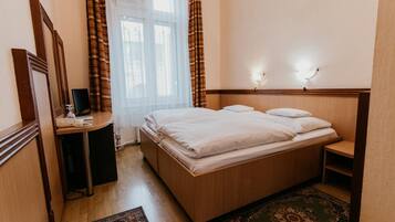 Habitación de hotel con una cama de madera, un escritorio con una silla, un espejo y una ventana con cortinas.