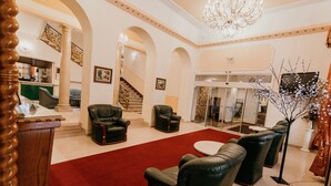A lobby with black leather chairs, a red carpet, a chandelier, and a staircase. - Tisza Hotel (Szeged)