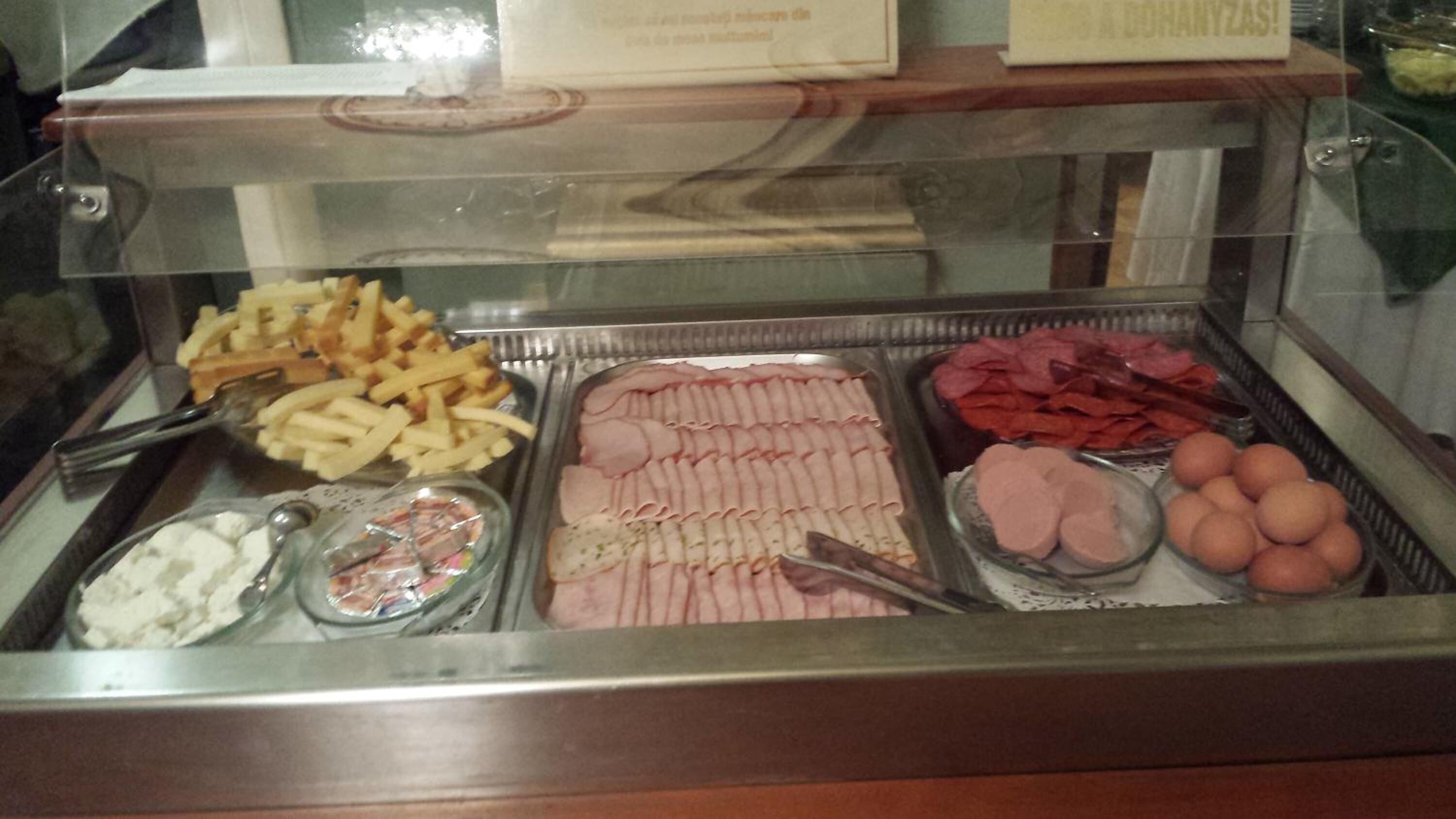 Un bufé con diversos alimentos, como papas fritas, carnes rebanadas y huevos.
