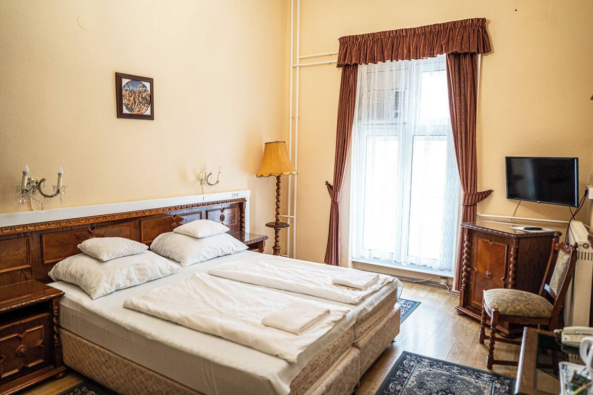 Habitación de hotel con una cama grande, televisión, escritorio con silla y ventana con cortinas.