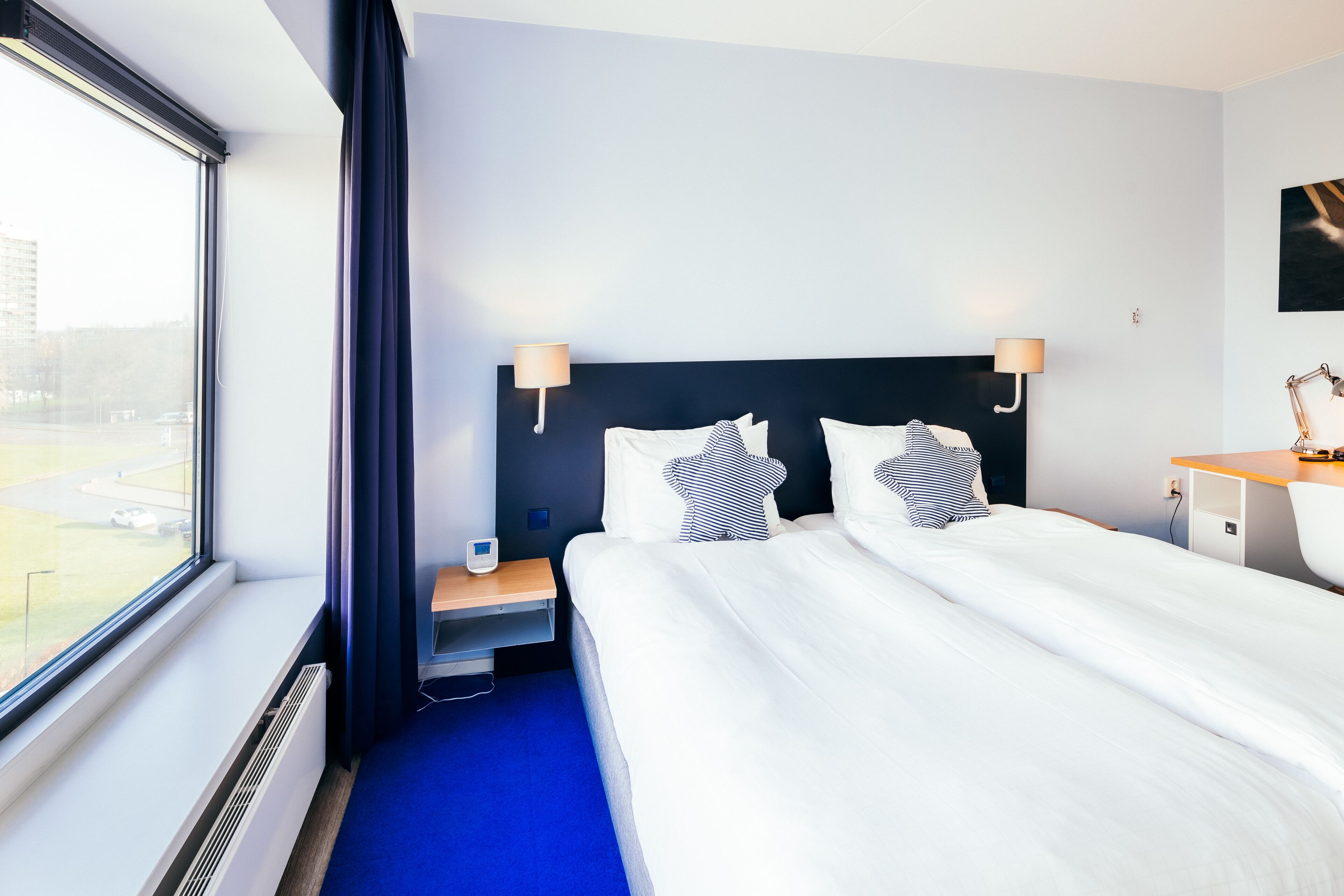 Una habitación de hotel con una cama grande, dos mesitas de noche, un escritorio y una ventana con cortinas.