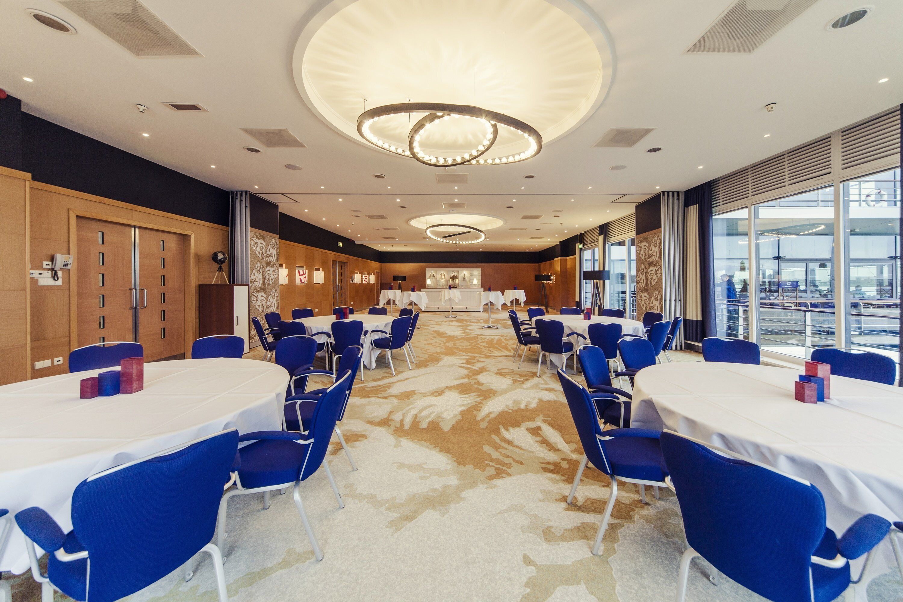 A conference room with round tables, blue chairs, and a large window offering a view of the outside.