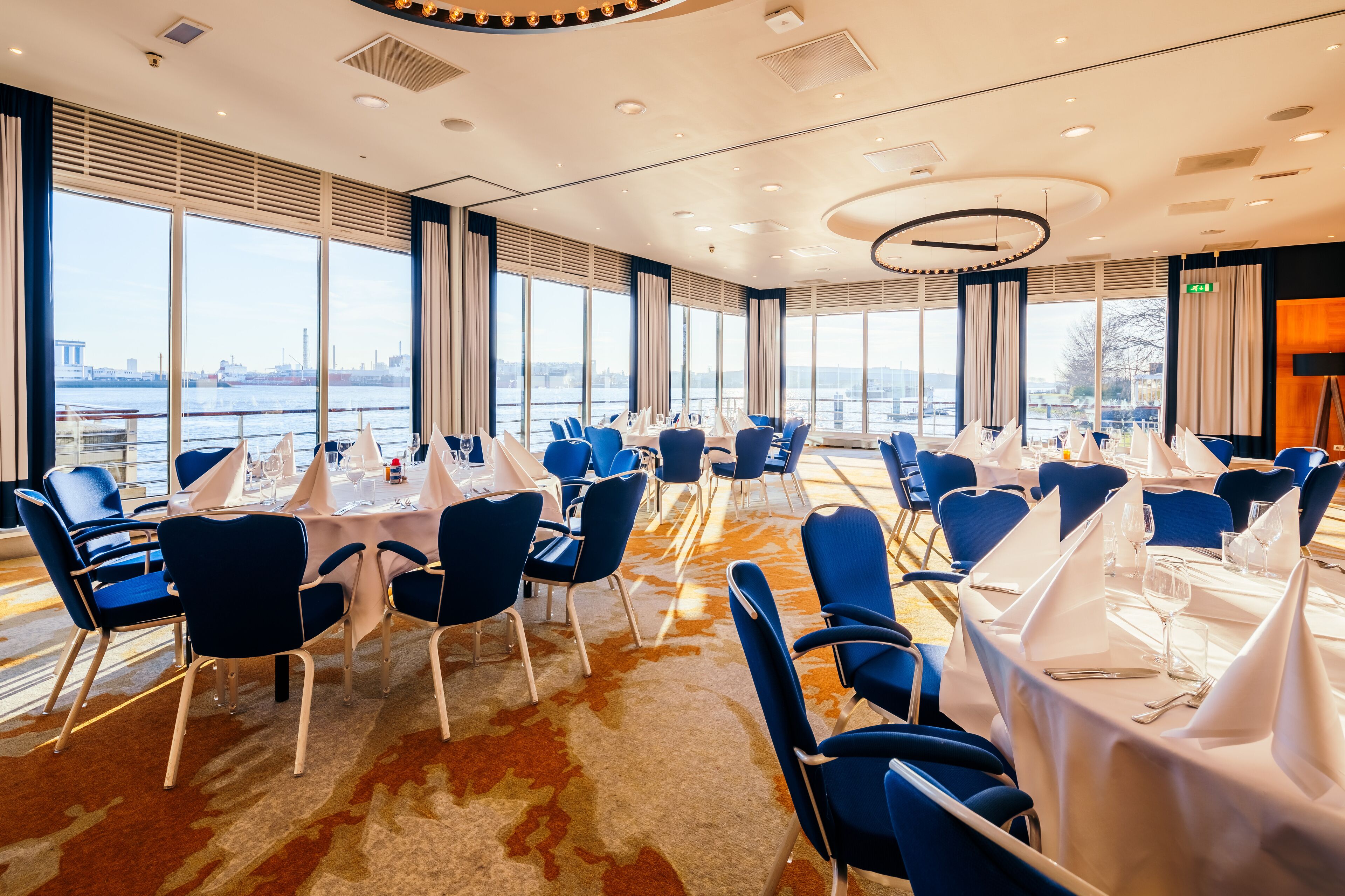A conference room with round tables, blue chairs, and large windows overlooking a river.