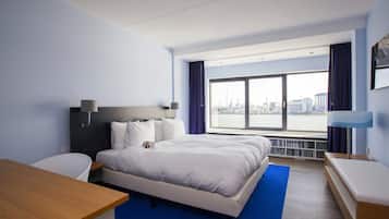 Ein modernes Hotelzimmer mit einem großen Bett, einem Schreibtisch und Blick auf die Stadt durch ein großes Fenster.