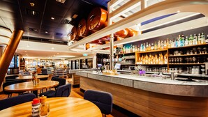 Un área de bar moderna con mesas redondas, una barra y estanterías llenas de botellas y vasos.
