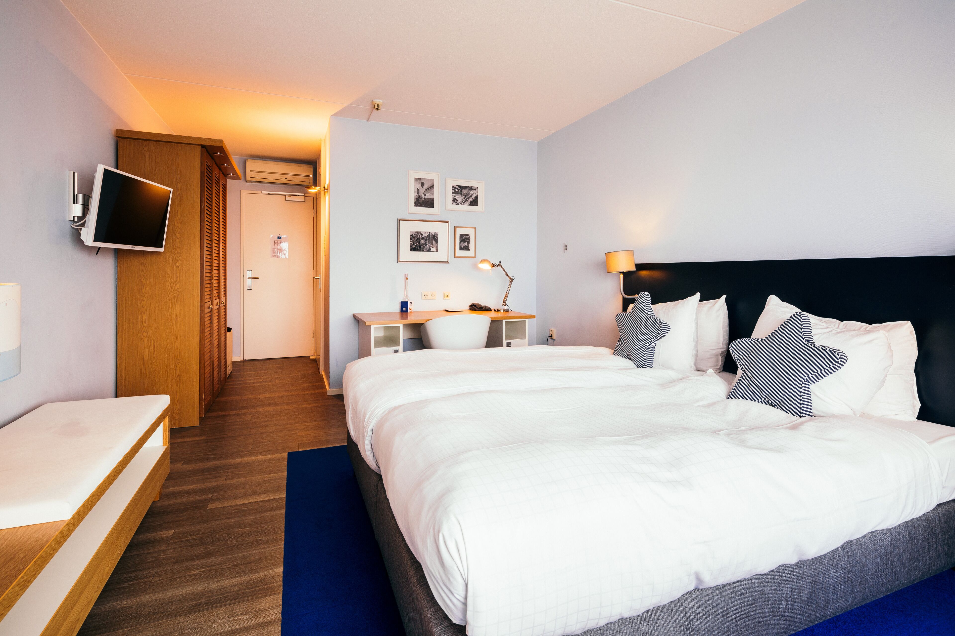 A hotel room with a bed, a desk, a TV, and a door.
