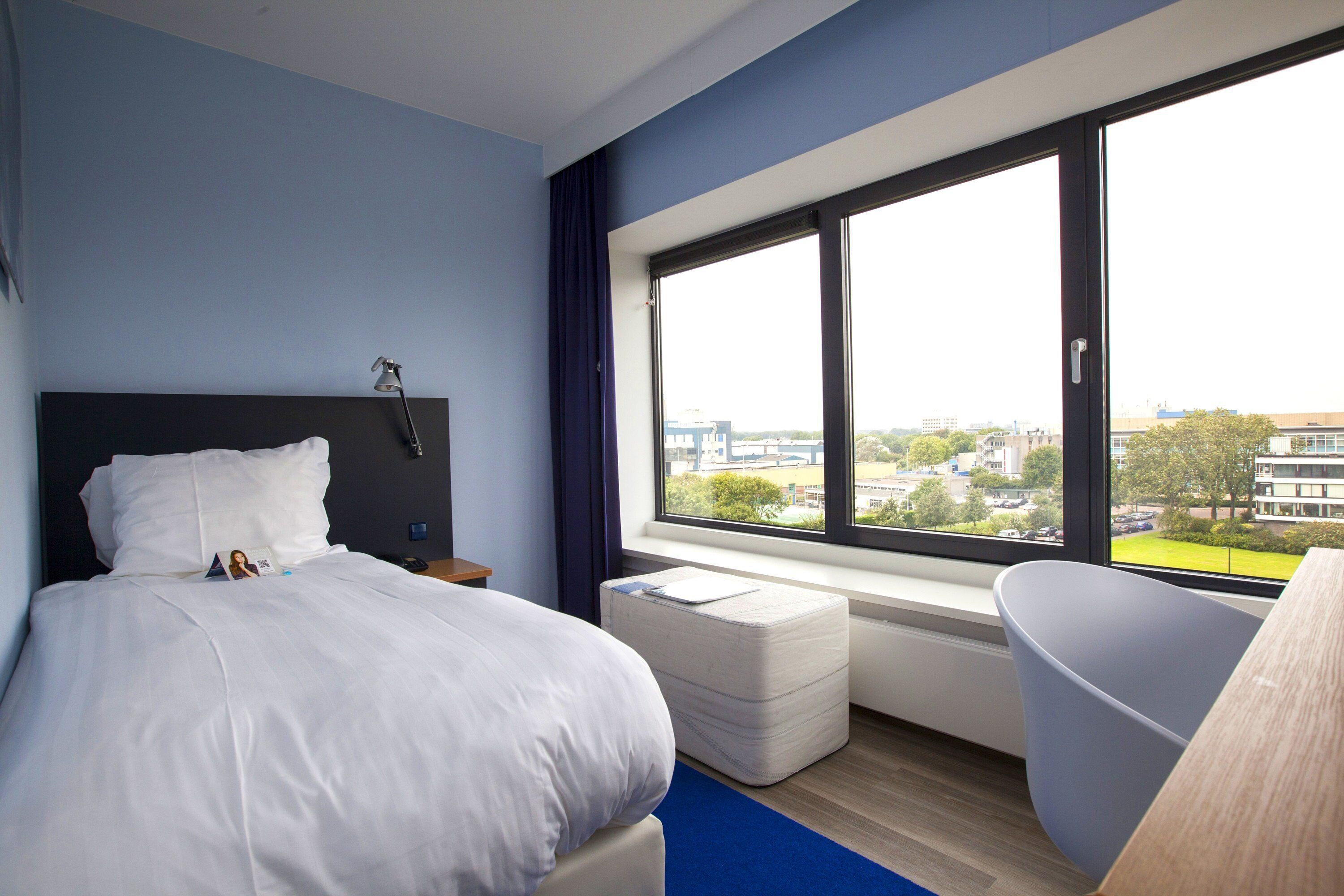 Una camera d'albergo con un letto, una finestra vista città, una scrivania e una sedia.