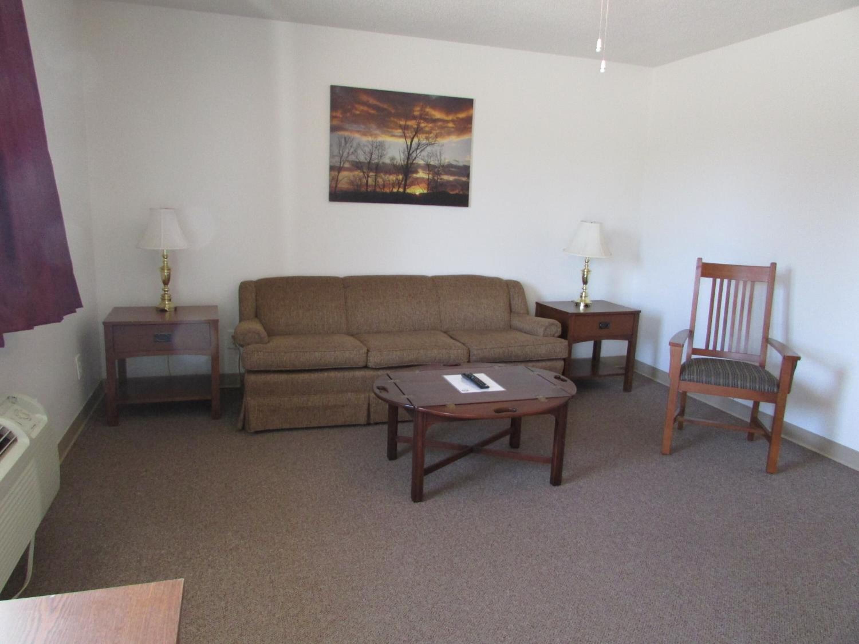 A living room with a sofa, two side tables, a chair, and a painting on the wall.