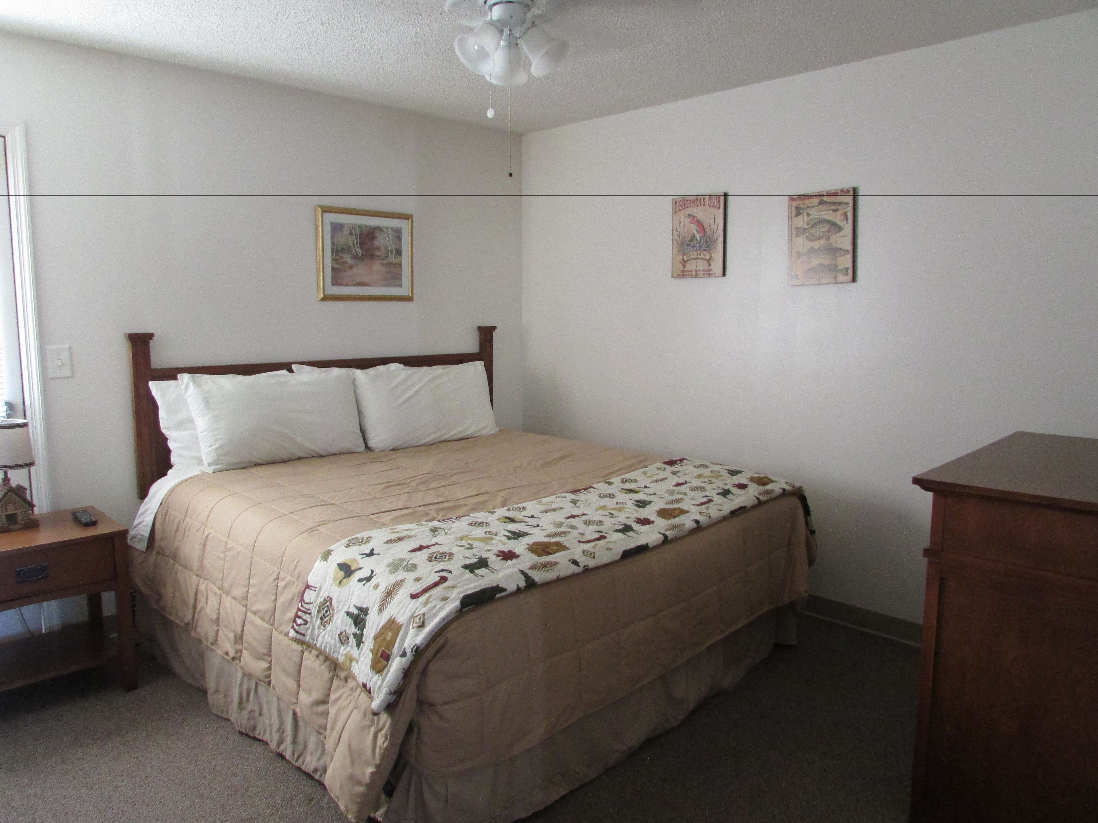 A bedroom with a bed, a nightstand, a dresser, and a ceiling fan.