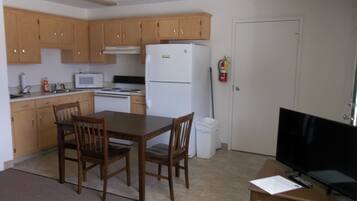 A compact kitchen with wooden cabinets, a white refrigerator, a microwave, and a dining table with chairs.