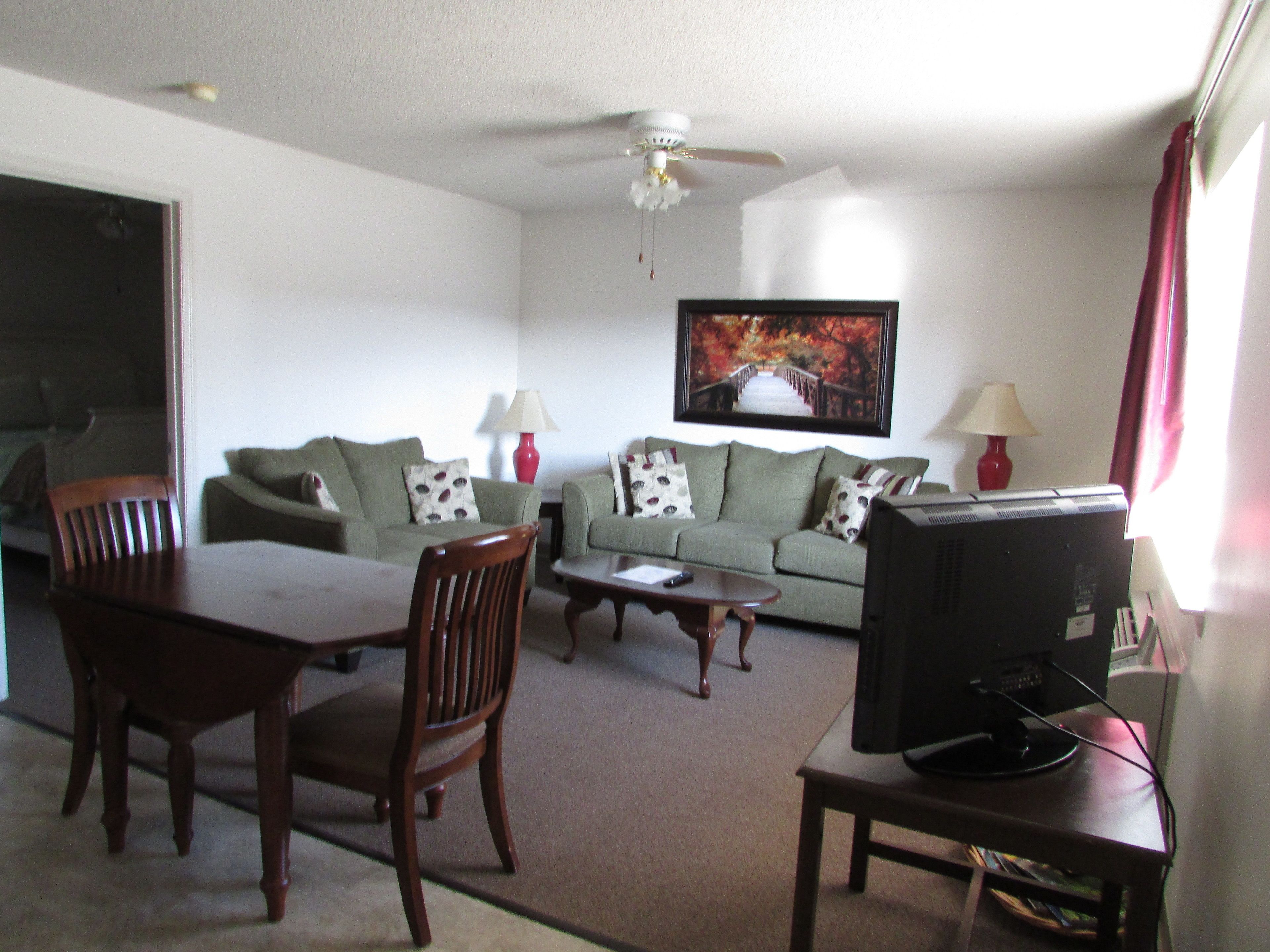 A living room with a sofa, two chairs, a coffee table, a television, and a ceiling fan.