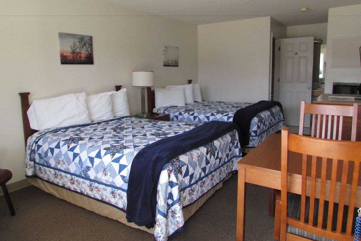 A hotel room with two beds, a desk, and a chair.