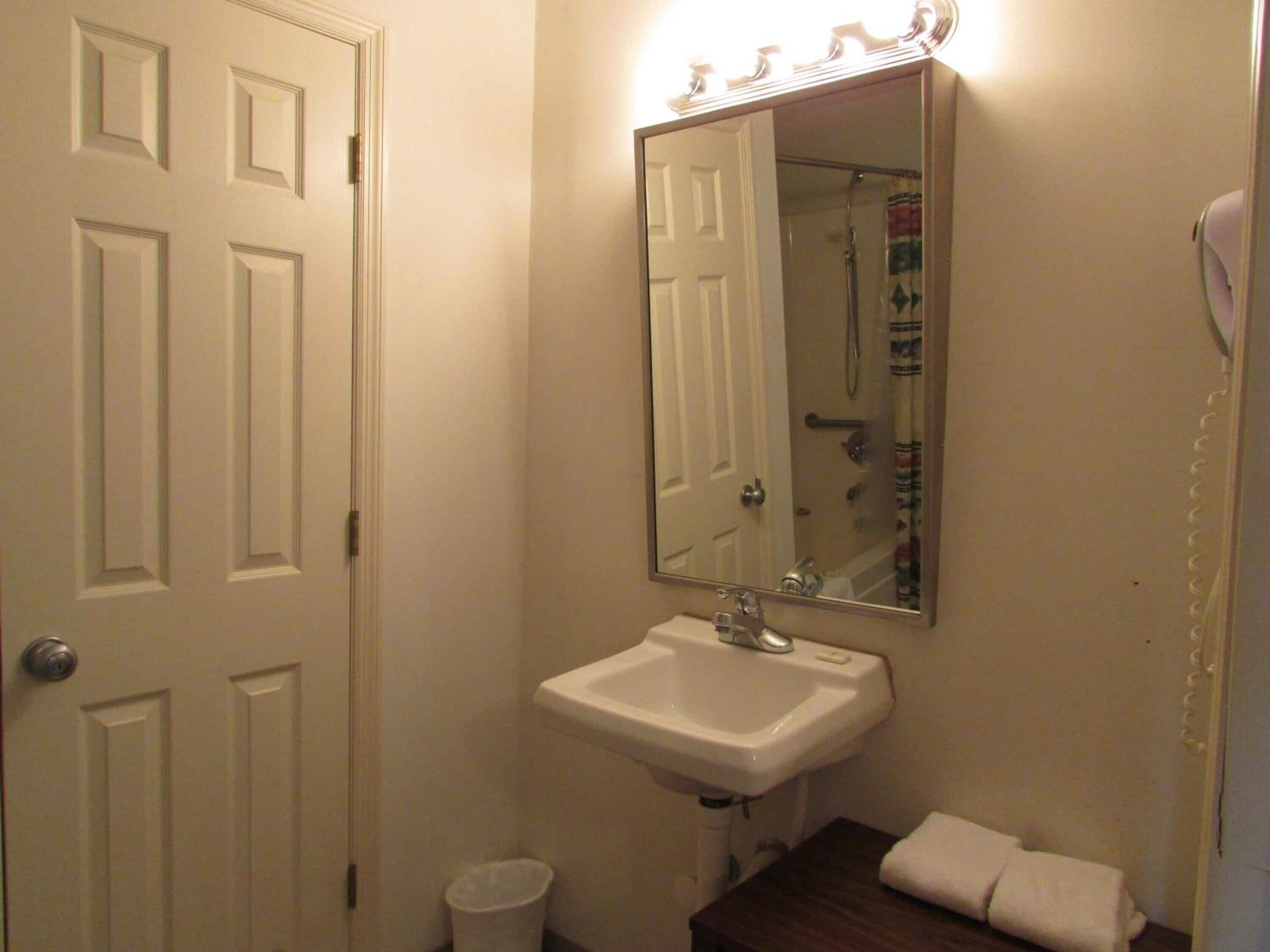 A bathroom with a white sink, a mirror, a shower, and a towel on the floor.