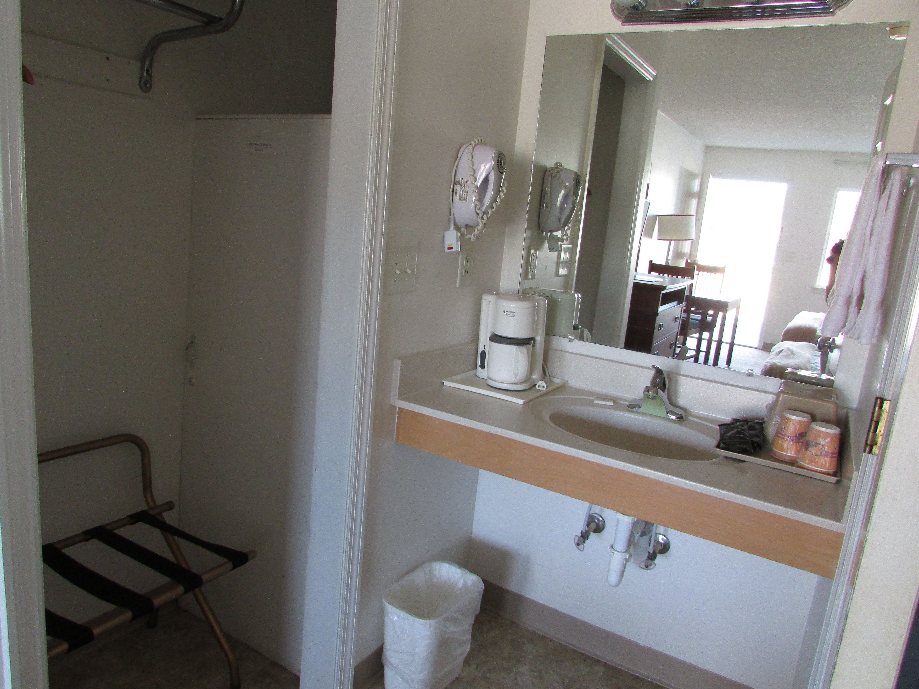 A bathroom with a sink, mirror, hairdryer, and a trash bin.