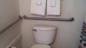 Une salle de bain standard équipée de toilettes, d’une barre d’appui et de deux serviettes suspendues à un porte-serviettes.