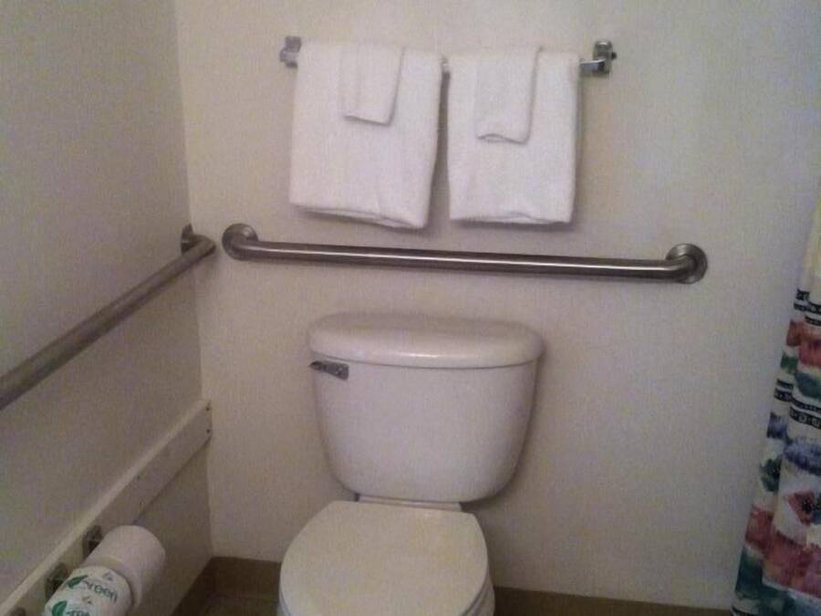 Une salle de bain standard équipée de toilettes, d’une barre d’appui et de deux serviettes suspendues à un porte-serviettes.