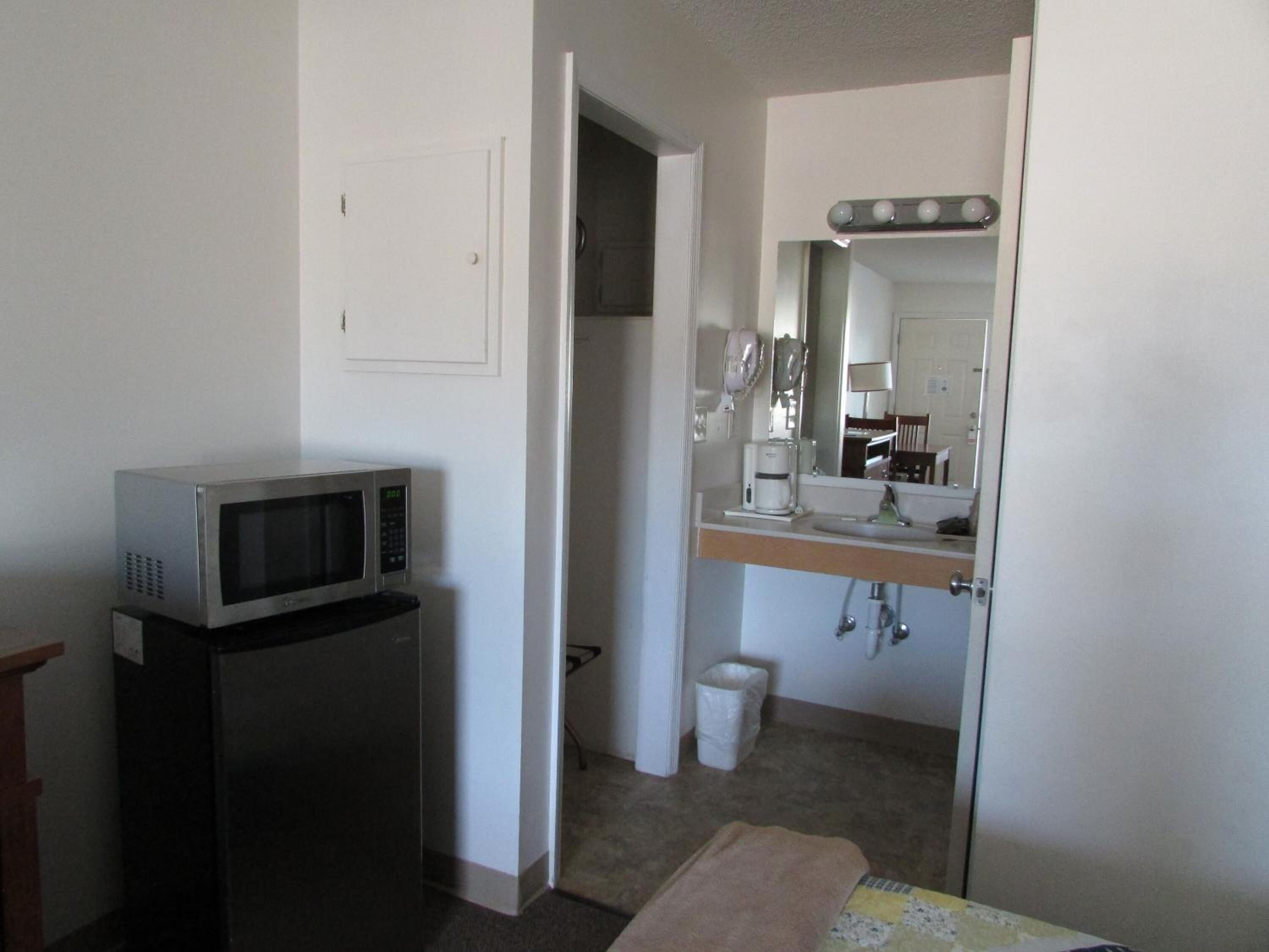 Habitación de hotel con kitchenette, que incluye un microondas, una cafetera y un lavamanos con espejo.